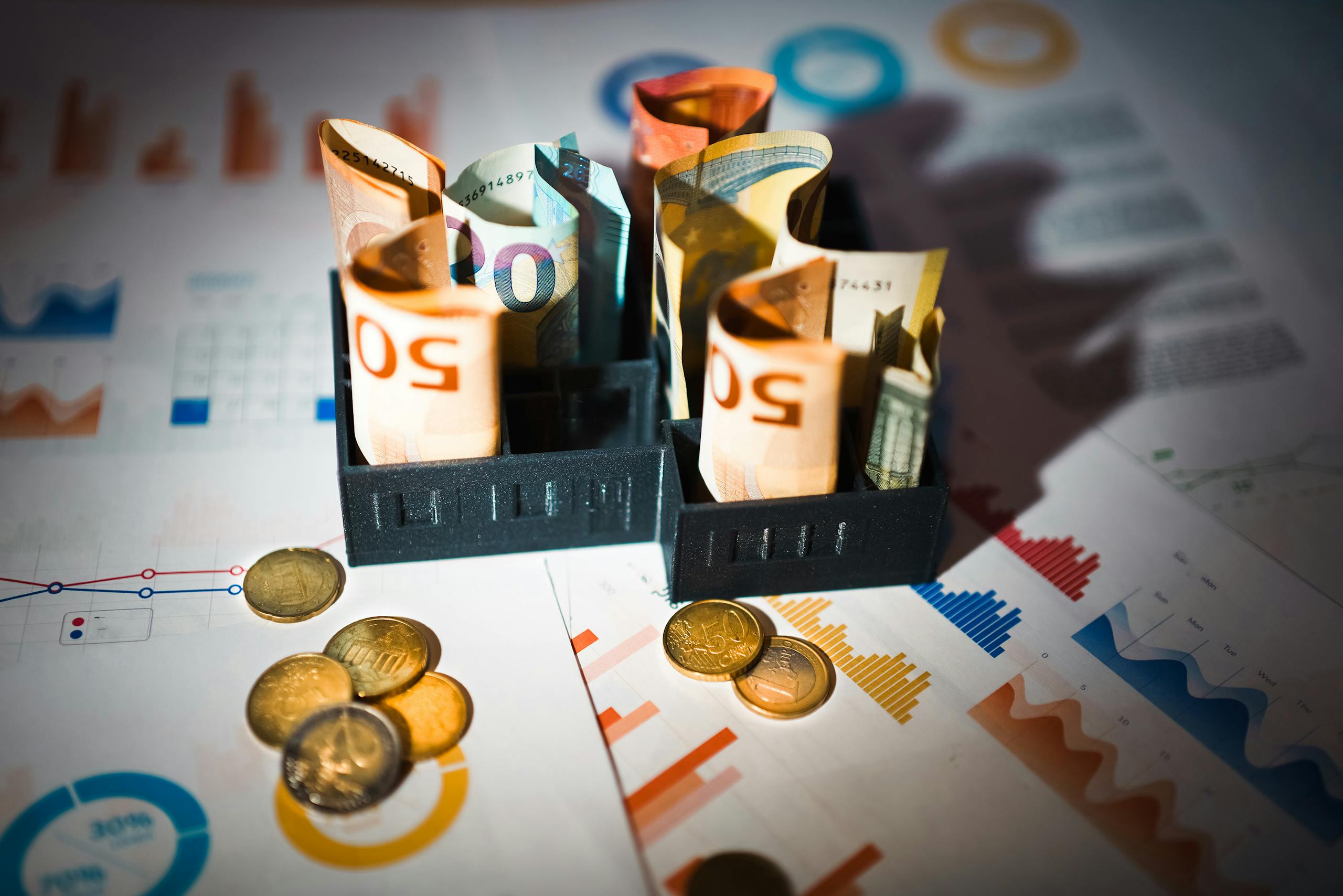A close-up of euro banknotes and coins on top of financial charts symbolizing investment and economic analysis.
